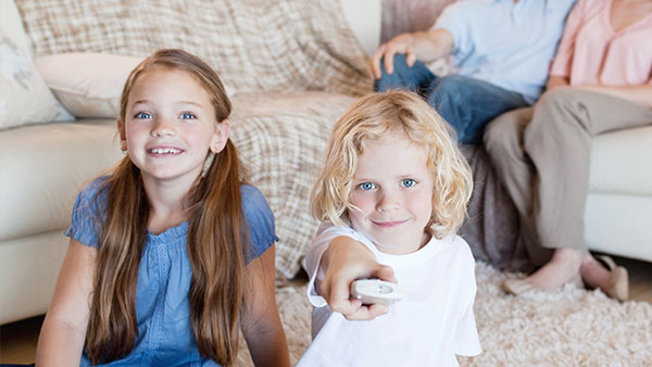 Two children watching tv with a remote control.